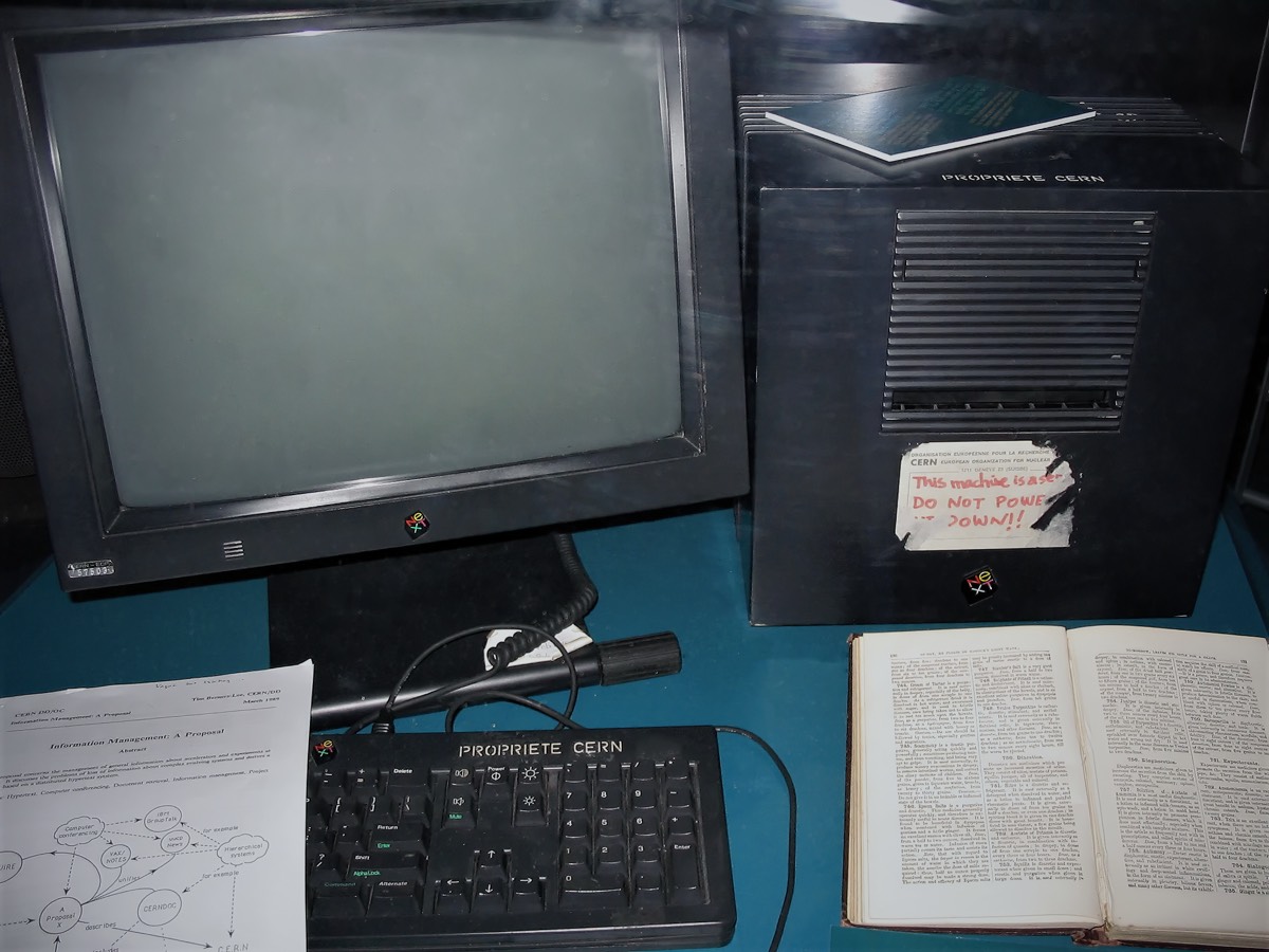 Le premier serveur web du monde, un ordinateur NeXT noir, exposé dans une vitrine du CERN. Une étiquette manuscrite à l’encre rouge est collée sur le boîtier : « This machine is a server. DO NOT POWER IT DOWN!! ». Devant la machine sont posés le document de proposition de 1989 et son schéma.